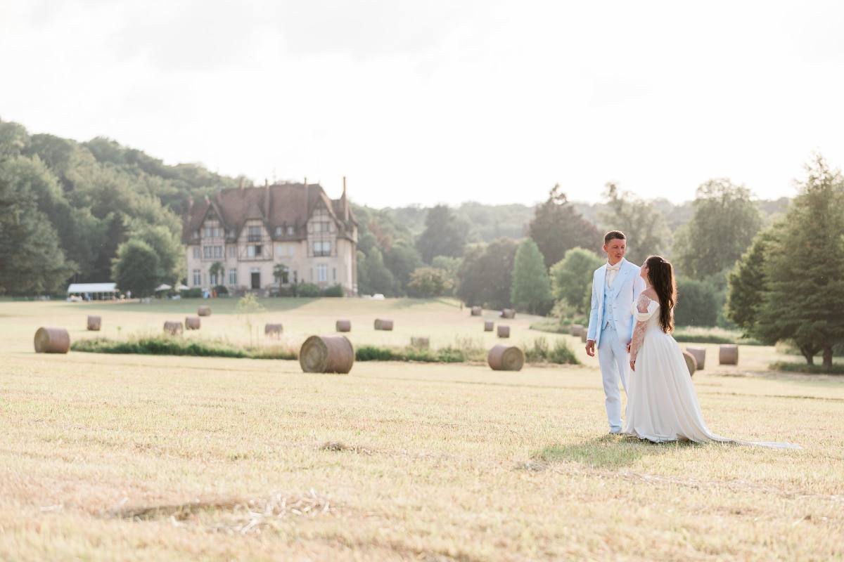 Bride and groom standing in hay field with château and trees in background