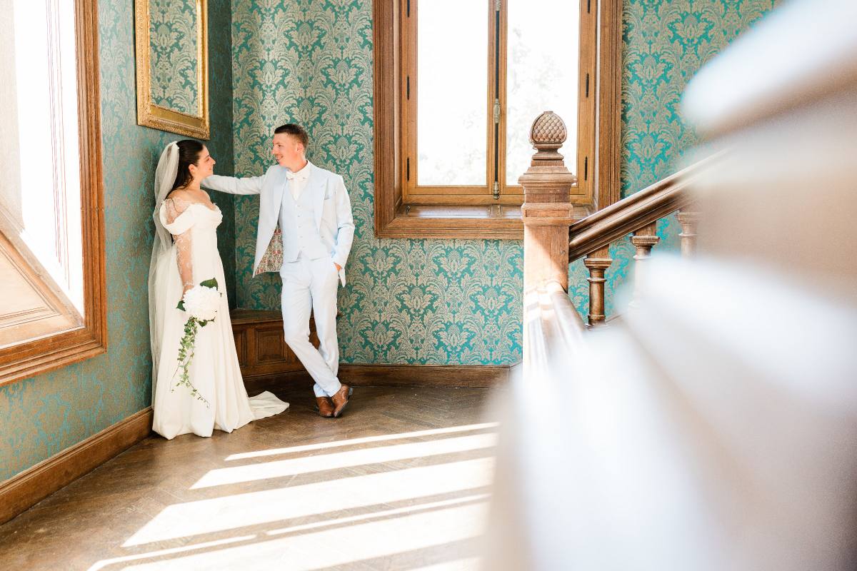 Une mariée et un marié se regardent dans un couloir élégant aux murs turquoise damassés.