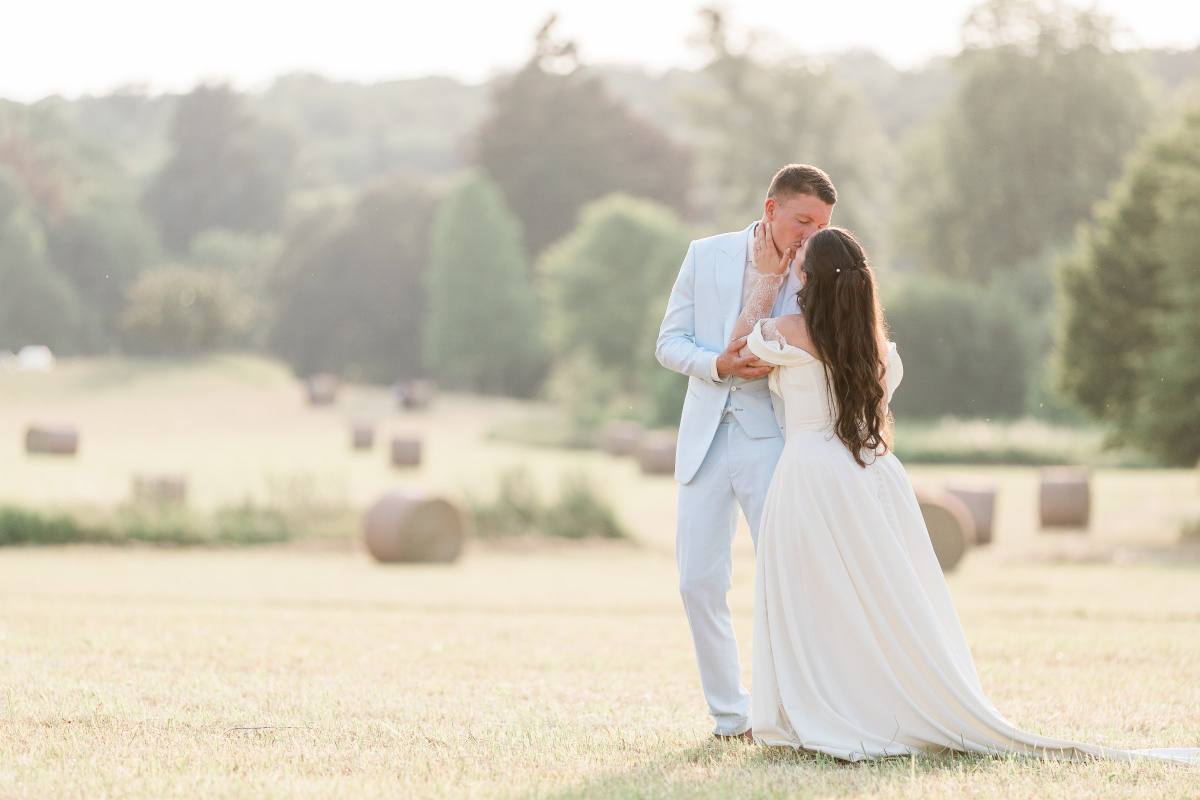 Un couple en tenue blanche se tient dans un champ doré avec des arbres en arrière-plan.
