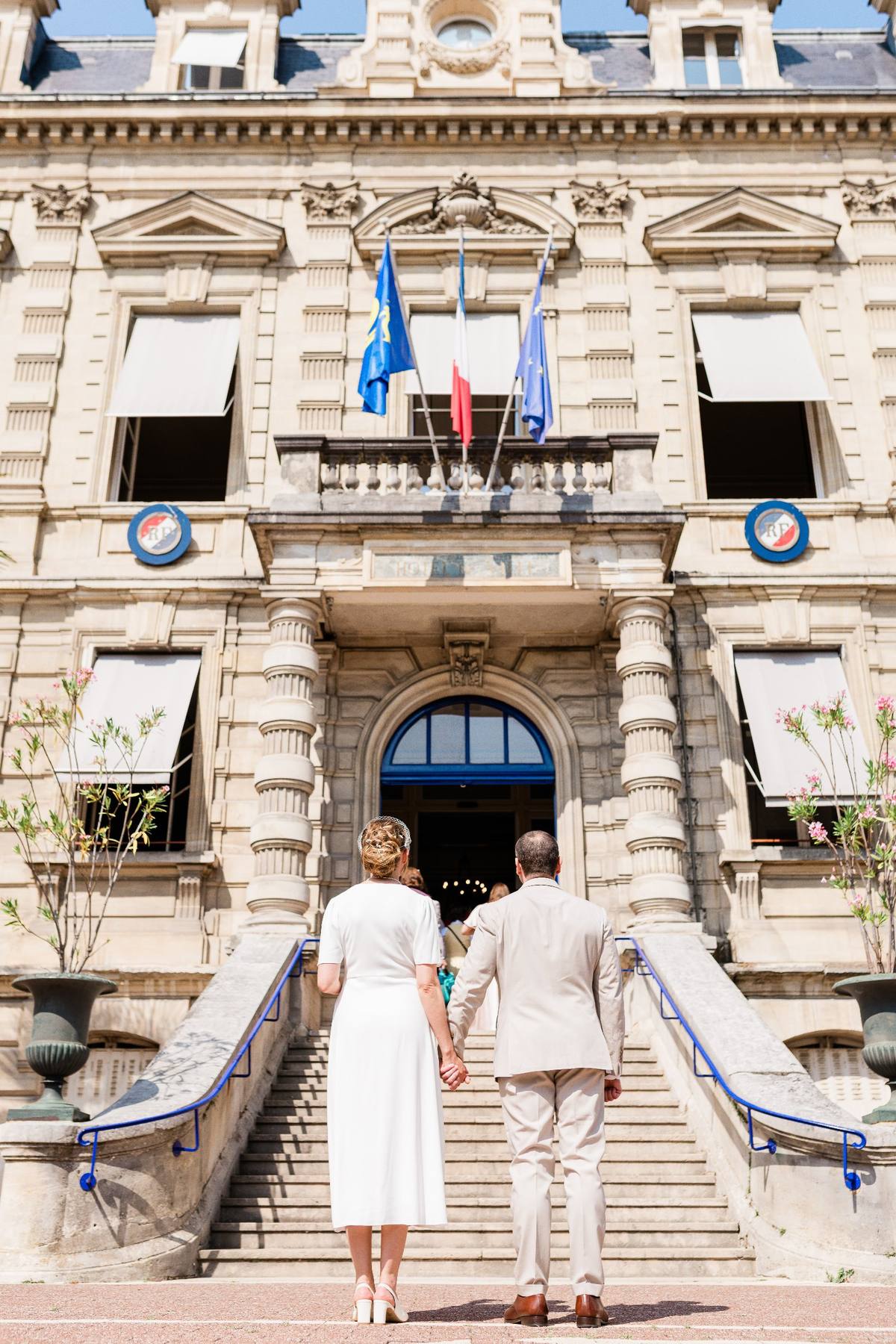 Couple de dos montant les escaliers d'un bâtiment officiel avec drapeaux bleus et blancs