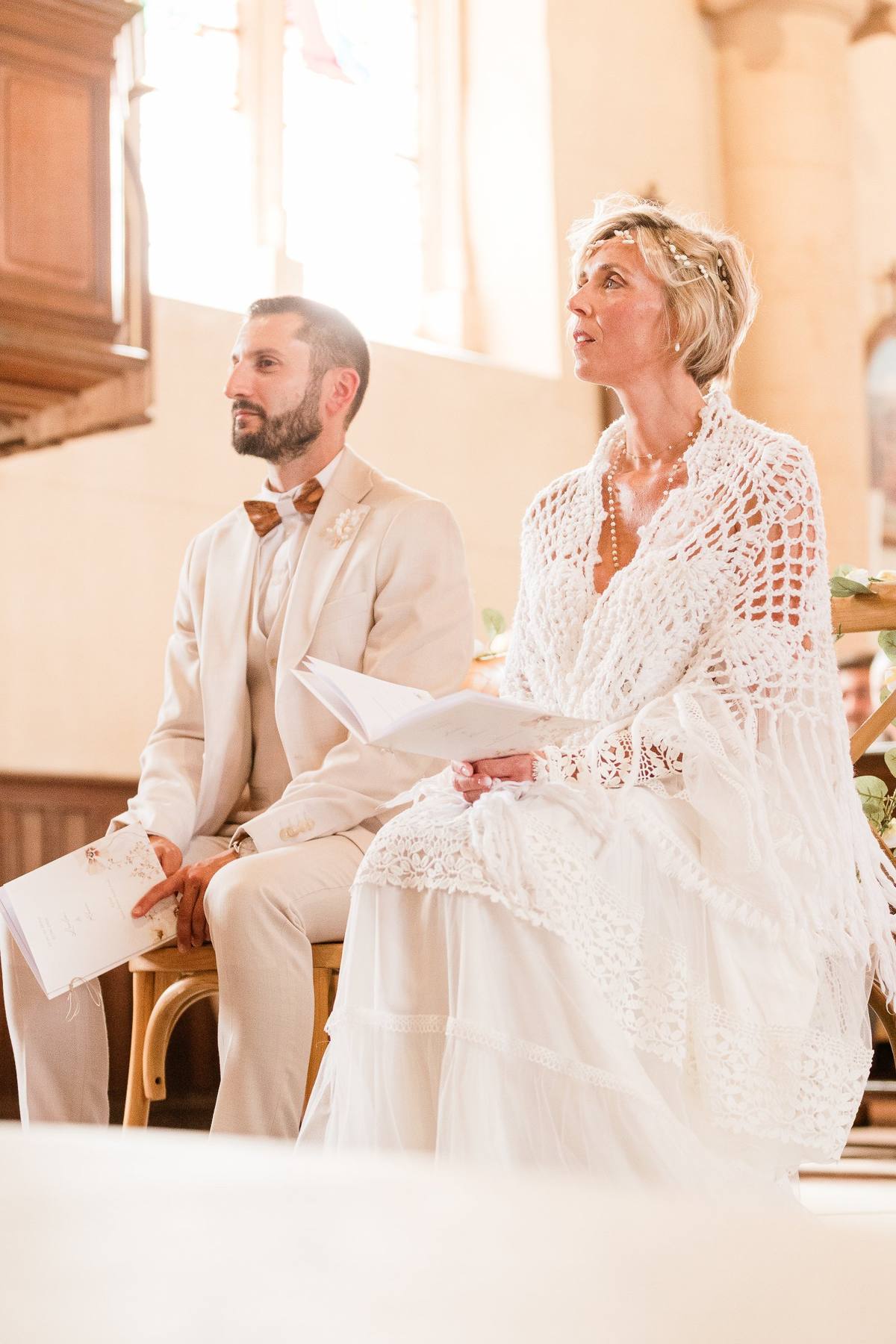 Couple in formal attire sitting together in a sunlit church during a wedding ceremony