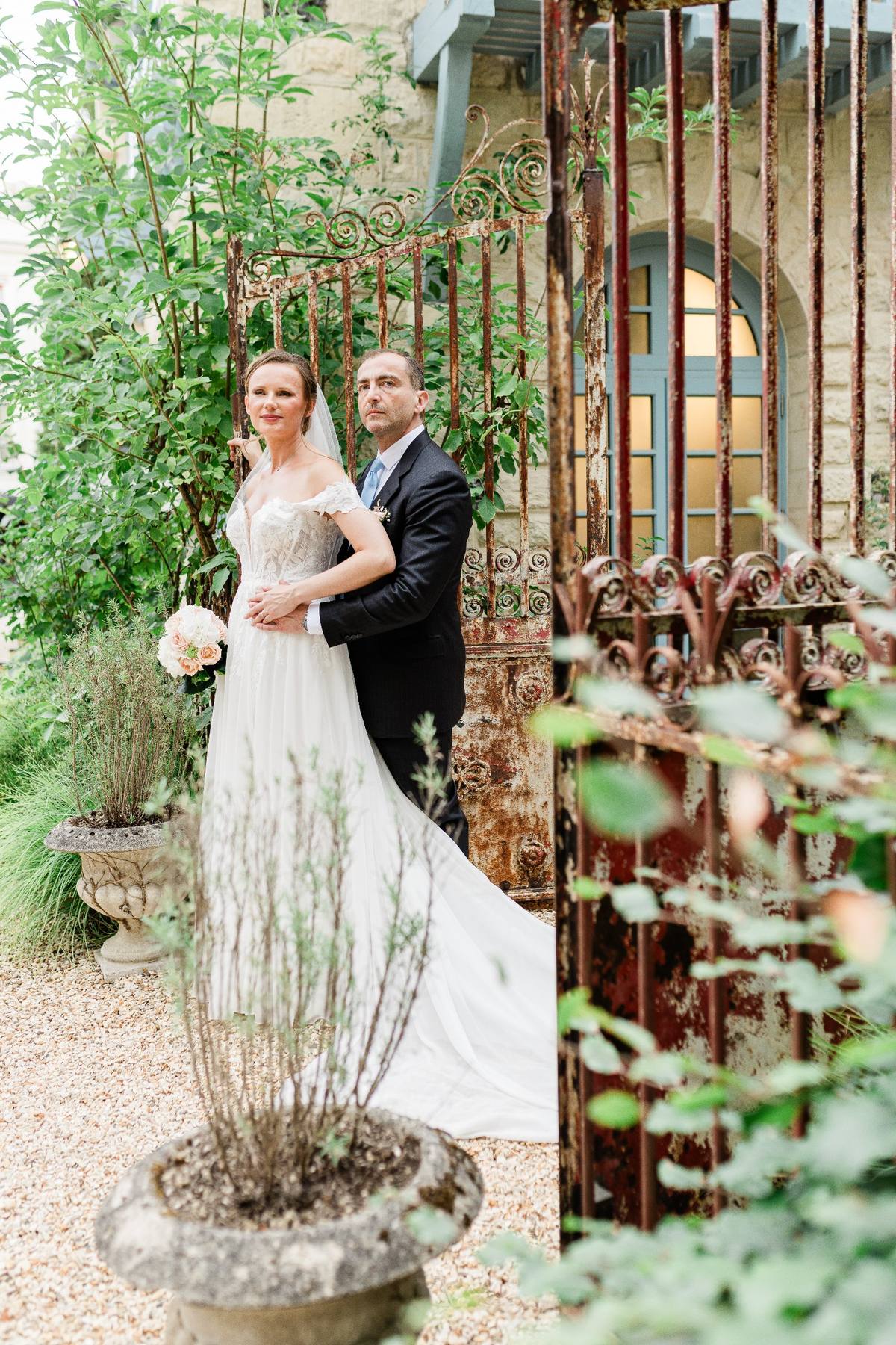 Bride and groom posing in a garden courtyard with rusty ornamental gates and climbing ivy.