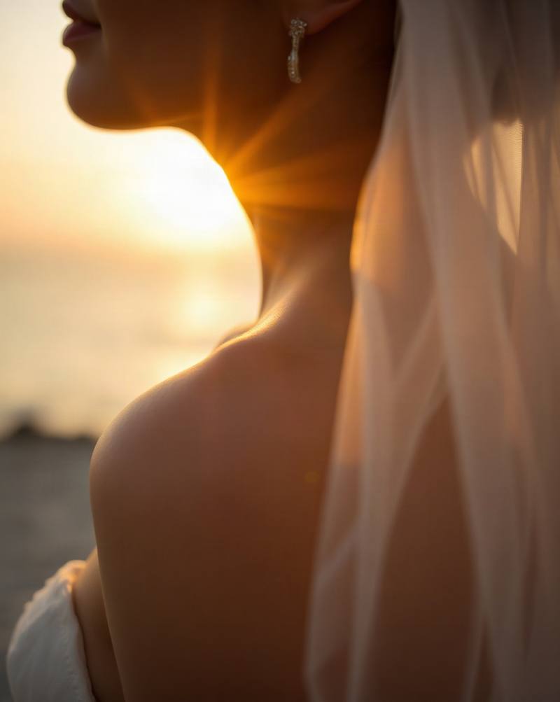 Woman in white dress silhouetted against golden sunset over water, wearing earrings.